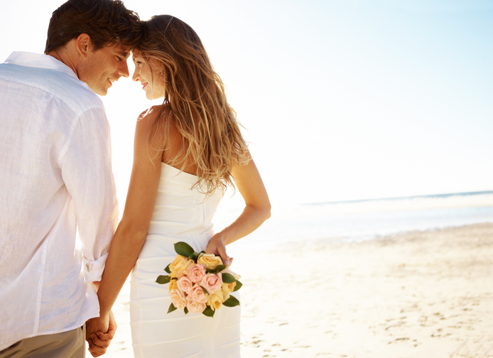 A young couple standing head-to-head on the beach while the woman holds flowers