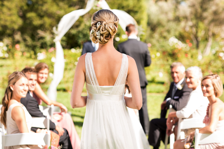 Rear view of young bride walking down the aisle while guests looking at her during wedding ceremony. Horizontal shot.