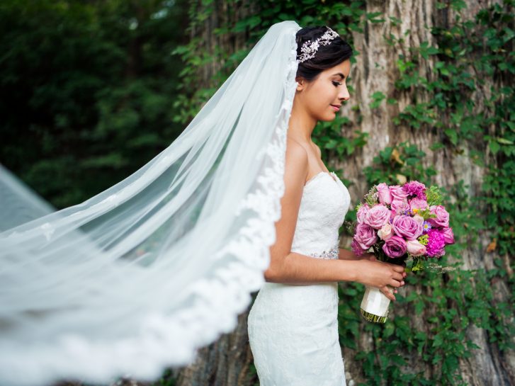 A beautiful young latin bride wearing a long veil and holding a flower bouquet.